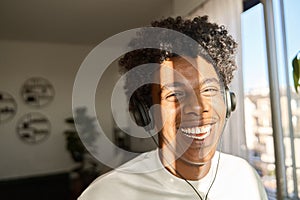 Happy gen z African American guy wearing headphones listening music at home.