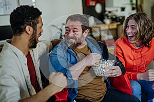 Happy German football fans friends watching football at home and eating popcorn.