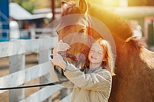 Happy ginger girl holding horse`s snout, touching horse`s head with hers