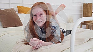 Happy ginger girl smiling on cozy bed at home