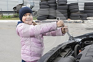 Happy girl - auto mechanic with a wrench is fixing a car. Repair service