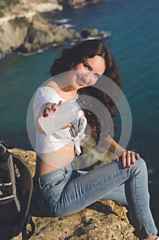 Happy girl backpacker is sitting on rock peak over sea