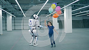 Happy girl with balloons is running around an anthropoid robot