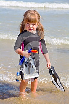 An happy girl on beach with colorful face masks and snorkels, sea in background