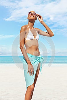 Happy girl at the beach side, wearing a sunglasses, bikini and pareo, portrait of African latin American woman in sunny summer day