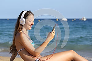 Happy girl in bikini listening to music using phone on the beach