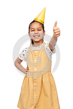 happy girl in birthday party hat showing thumbs up