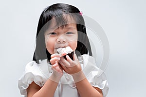Happy girl bits sweet chocolate cake. She wears white shirt. Sweet smiling. Children`s concept with eating sweets