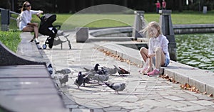 Happy girl blonde feeds pigeons in the park.