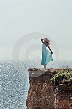 Happy girl in blue dress standing on edge cliff