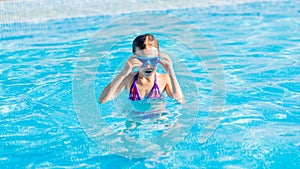 happy girl in blue goggles swimming in the swimming pool