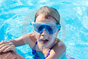 happy girl in blue goggles swimming in the swimming pool
