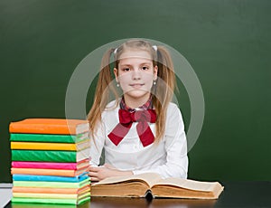 Happy girl with books near empty school green chalkboard