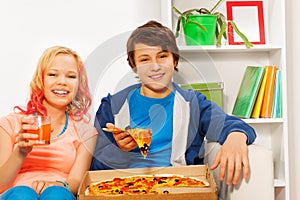 Happy girl and boy hold pizza pieces on white sofa