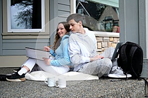 Happy girl and boy sit on a window ledge and drink coffee