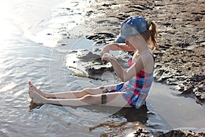 happy girl in a bright swimsuit sits in the river and plays with sand, active holidays with children on the beach in