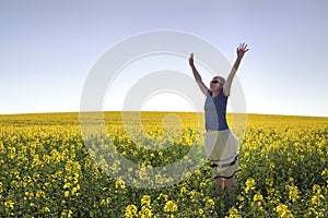 Happy Girl among Canola Plants under Blue Sky