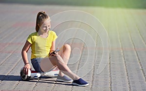 Happy girl child authentically reads messages on a smartphone while walking in a park on a hoverboard, authentic photo