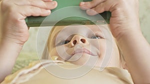 Happy girl child with blond hair and pigtails, lying on the sofa, using the phone, smiling, portrait