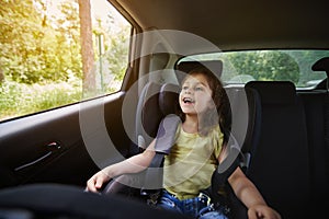 Happy girl in a child car seat wearing a seatbelt while traveling by car