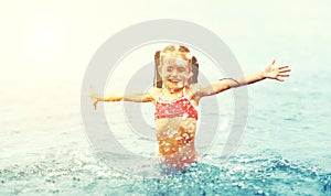 Happy girl child plays and swims with splashes on the beach