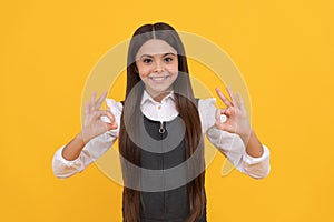 Happy girl child in school uniform smile gesturing double OK sings yellow background, okay