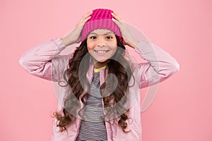 Happy girl child smile with beauty look and long brunette hair fixing fashion beanie hat on head pink background, autumn