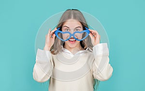 Happy girl child smiling in big funny heart-shaped glasses blue background