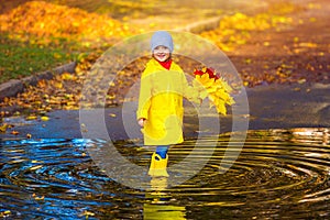 A happy girl child in a yellow raincoat and rubber boots in a puddle on an autumn walk