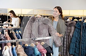 Happy girl chooses winter down jacket in clothing store