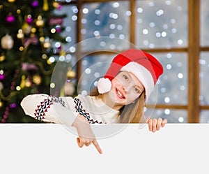 Happy girl in christmas hat peeking and pointing down at empty board