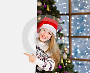 Happy girl in christmas hat peeking and pointing at empty board
