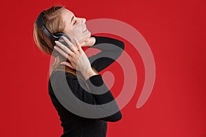 Happy girl, with closed eyes enjoying music in headphones and smiling. On a red background.