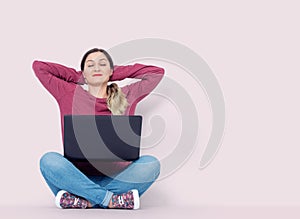 Happy girl with closed eyes sitting on the floor with a laptop relax in lotus pose, on light pink background