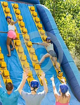 Happy girl competing in climbing with wood poles on inflatable slide