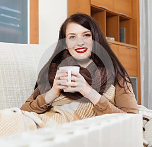 Happy girl with cup near heater