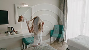 Happy girl dancing front mirror in resort hotel bedroom. Cheerful girl shaking head and hair front mirror. Teenager girl