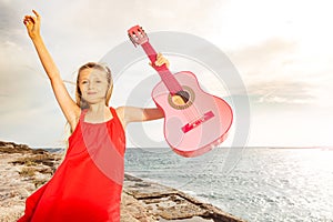 Happy girl dancing and playing guitar by the sea