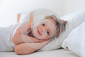 Happy girl daughter waking up smiling looking at camera on parent`s bed at morning. Happy relaxed family life with