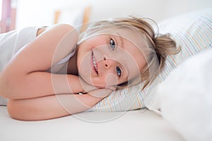 Happy girl daughter waking up smiling looking at camera on parent`s bed at morning. Happy relaxed family life with