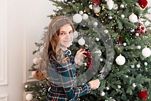 Happy girl decorate the Christmas tree. Portrait smilling redhead little girl near Xmas tree. Christmas celebration. Child decorat