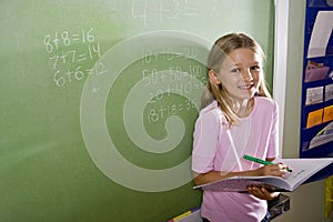 Happy girl doing math on blackboard in class