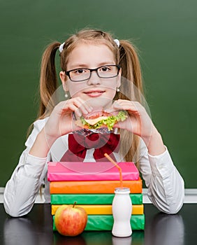 Happy girl eating sandwich near empty green chalkboard