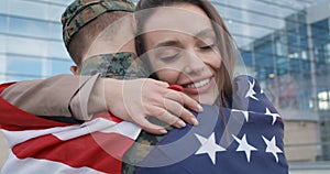 Happy girl embracing military boyfriend covered with american flag.