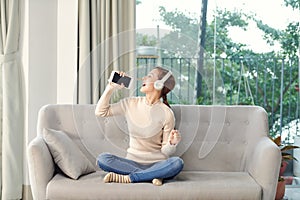 Happy Girl Enjoying Music In headphone And Singing Favourite Song, Relaxing On Sofa