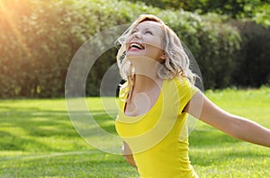 Happy girl enjoying the Nature on green grass. Beautiful young woman smiling with arms outstretched