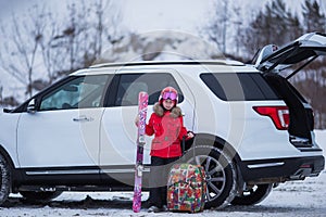 Happy girl enjoying winter sports  cheerful portrait of a girl next to the car and in a ski mask  arrived at the ski resort 