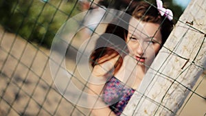 Happy girl with flower in hair posing at fencing on beach looking in camera. Sun