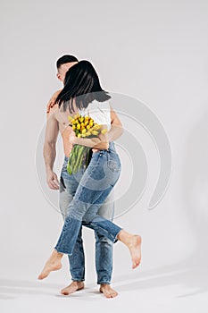 A happy girl with flowers and her boyfriend with naked torso, they are dancing, having fun. Attractive young woman and