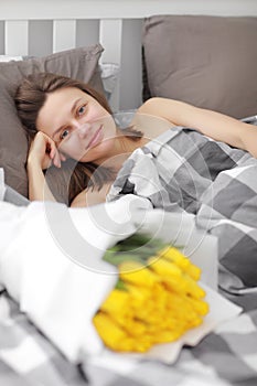 Happy Girl with flowers yellow tulips lying on a bed with enjoying flowers and romantic gift in Valentine day. She just woken up